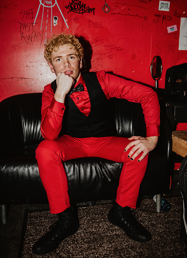 fluffio poses in red outfit in red room wearing bowtie at Lee's Palace in Toronto
